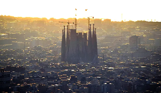 The basilica and its cranes standing out above the hazy rooftops of Barcelona in the golden light of sunrise