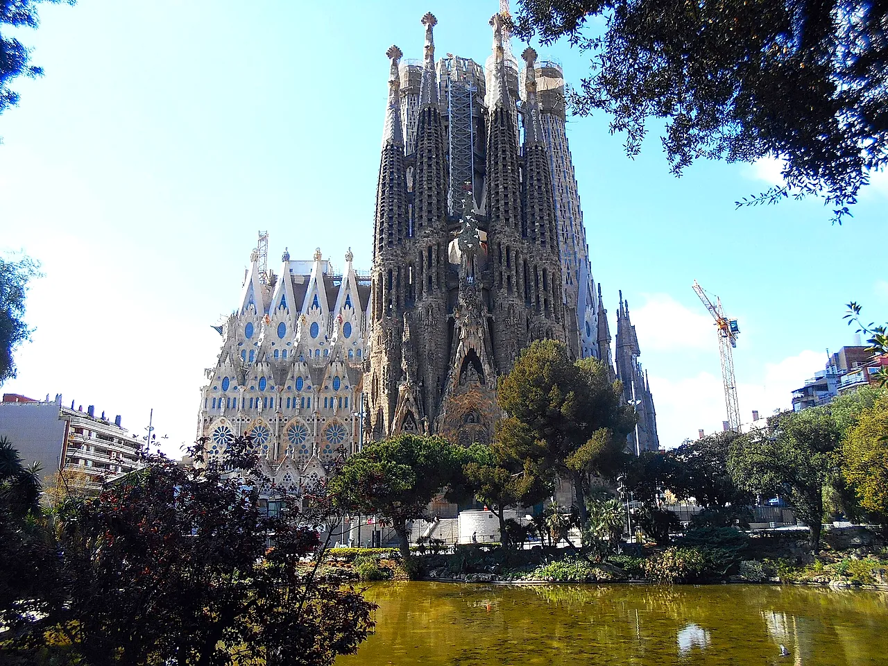 La basilica con le sue alte torri che spuntano dietro gli alberi e lo stagno del piccolo parco, con una gru sulla destra