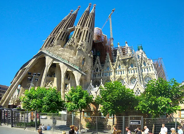 General view of the Passion facade side of the basilica from the street, with trees in the foreground and the towers above