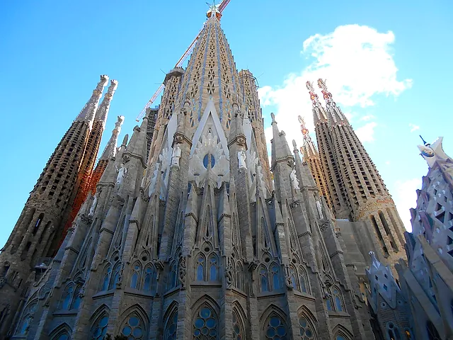 Looking up at the pinnacled towers of the basilica from the foot of the building, with a crane and blue sky above