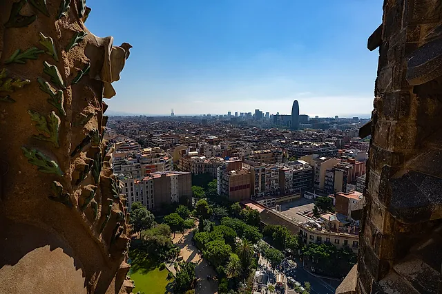 View over the Eixample grid and the distant skyline of Barcelona from a tower of the Nativity facade, framed by carved stone foliage